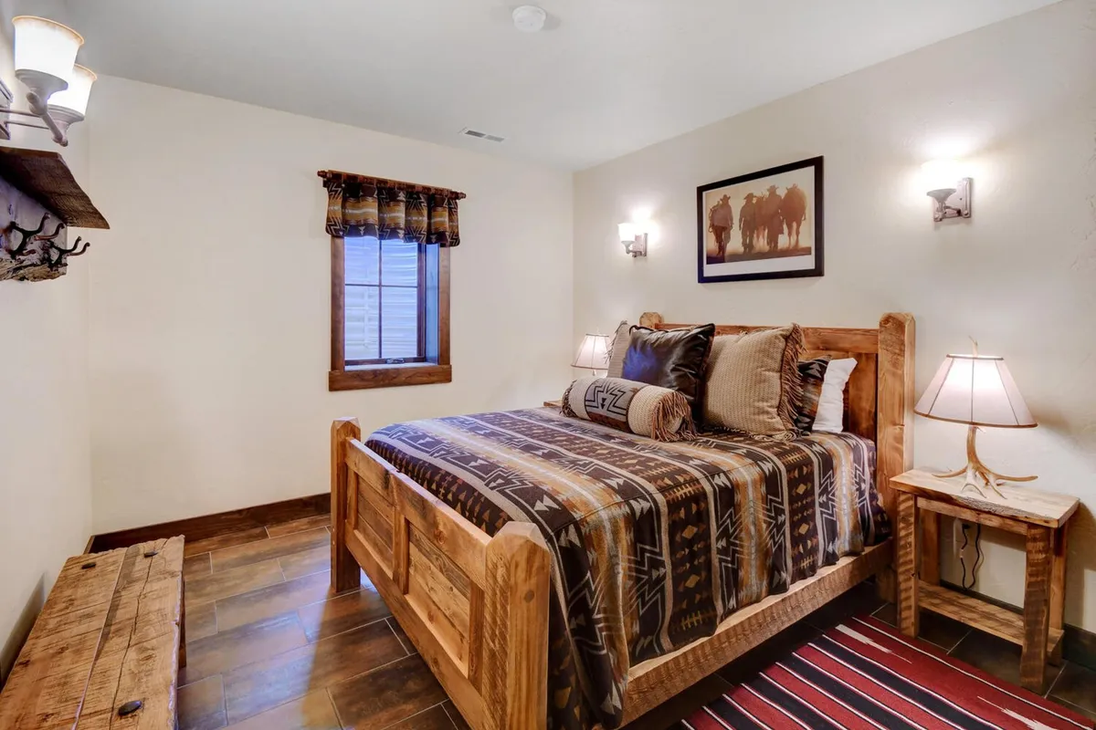 A serene bedroom featuring a cozy bed with premium bedding, framed artwork above the headboard, a window allowing in natural light, and a nightstand with a lamp and a soft rug underfoot. The space radiates warmth and tranquility, inviting restful sleep after a day of adventure.