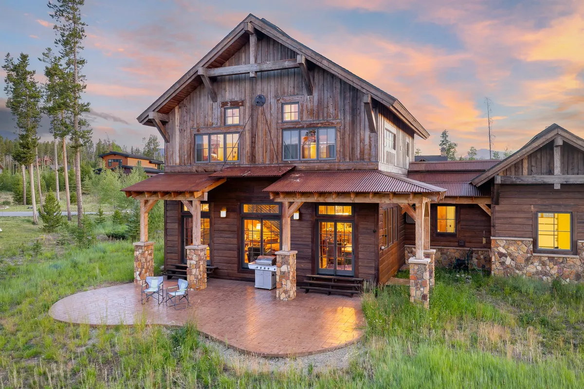 An exterior shot featuring a wooden facade with stone pillars, an outdoor seating area, and a barbecue grill. The patio is set up for outdoor dining and relaxation, inviting guests to enjoy the fresh mountain air. The ambiance is cozy and welcoming, perfect for gatherings or enjoying a grilled feast under the stars.