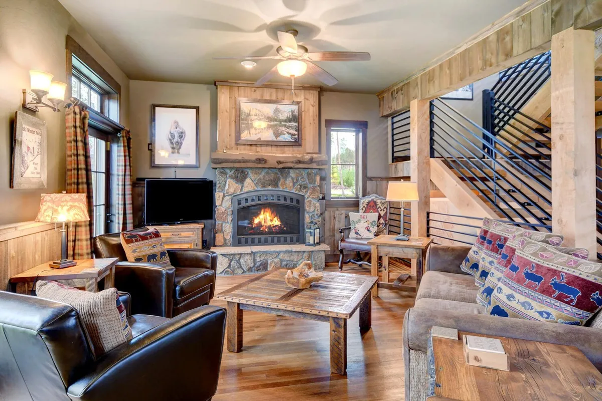 A sun-drenched living area featuring a custom stone fireplace with a cozy fire, a wooden coffee table, plush seating with decorative pillows, and large windows that let in abundant natural light. The layout is open and inviting, perfect for group gatherings, with space for both relaxing and socializing.
