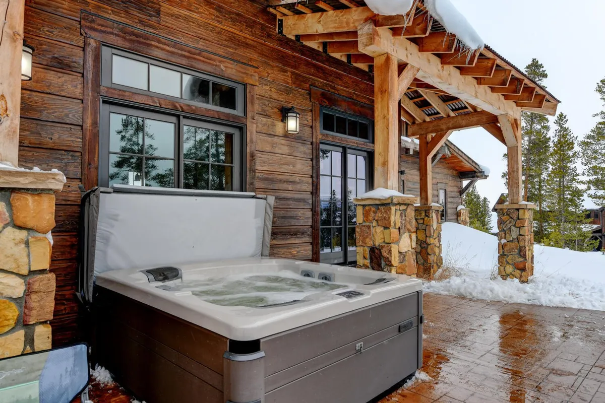 This exterior shot centers on the property's outdoor hot tub, framed by sturdy wooden beams and stone columns. The hot tub offers sweeping views and embodies relaxation and opulence, ideal for unwinding after curated adventures or enjoying alpenglow sunsets in privacy.