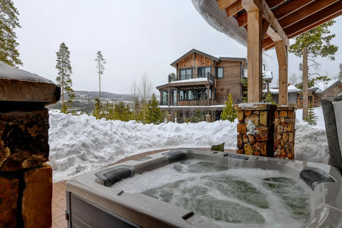 A tranquil outdoor setting with a private hot tub overlooking a snowy landscape and a wooden house. The inviting scene hints at relaxation after a day of adventure, with panoramic mountain views enhancing the luxurious comfort of the home base.