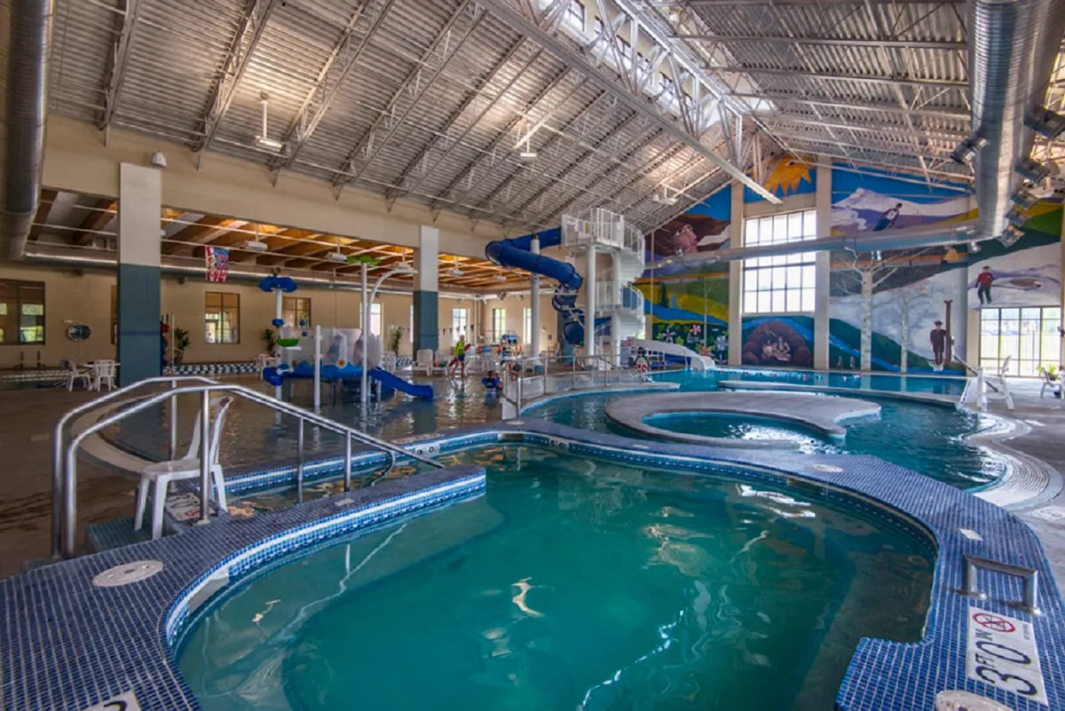 This image features a lively interior of a recreation center with a large pool area, colorful murals, and water slides. Children are playing in the pool, and families are gathered around, enjoying the vibrant, energetic atmosphere.