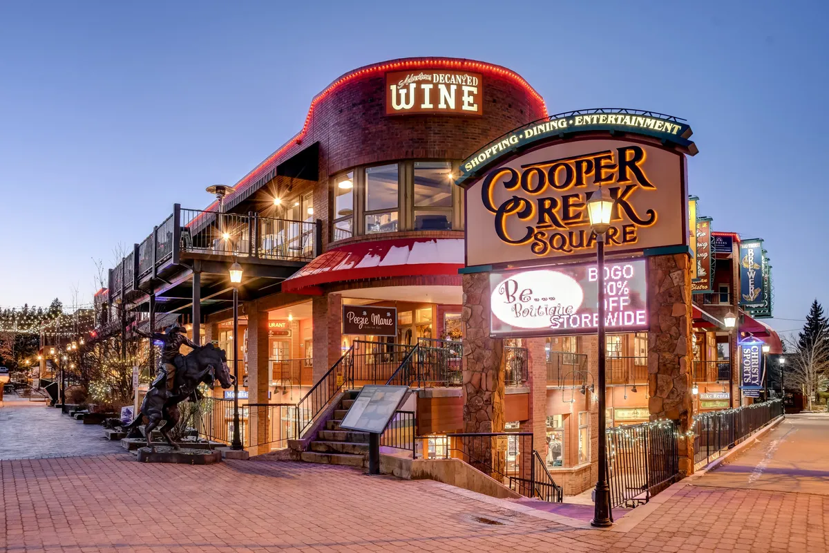 This dynamic exterior image features Cooper Creek Square's sign, vibrant wine shop signage, an inviting outdoor seating area, and festive decorative lighting. It hints at the lively downtown scene, showcasing opportunities for fine dining, shopping, and entertainment steps from the luxury retreat.